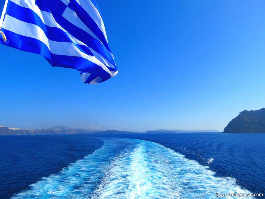 The Greek flag fluttering from the wind and white foam from the ferry