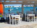 Taverna with white chairs and tables and fishing boats in the sea